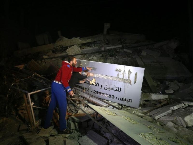Palestinian men point at an insurance company sign amid the rubble of a building that collapsed from reported Israeli strikes in Gaza City on March 25, 2019. 
MOHAMMED ABED / AFP
