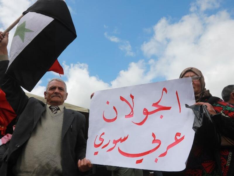Protesters hold a national flag and a placard in the town of Quneitra in the Syrian occupied Golan Heights, during a demonstration against the US decision to recognise Israel's sovereignty over the Israeli-annexed Golan Heights, on March 26, 2019. The placard reads in Arabic: "The Golan is Arab and Syrian". 
Louai Beshara / AFP