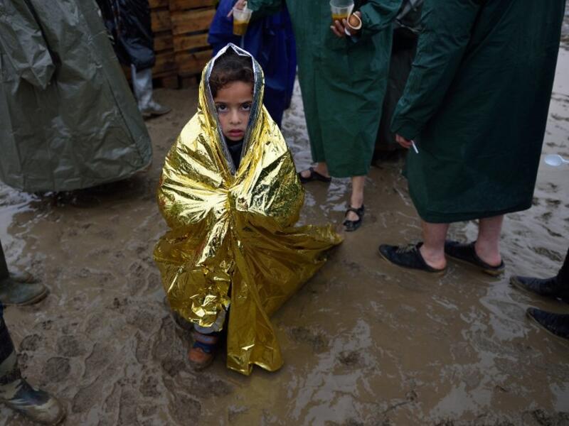 A child wrapped in a survival blanket looks as migrants queue for hot soup on March 13, 2016, in a makeshift camp at the Greek-Macedonian border, near the Greek village of Idomeni, where thousands of refugees and migrants are stranded by the Balkan border blockade. (AFP/Daniel Mihailescu)