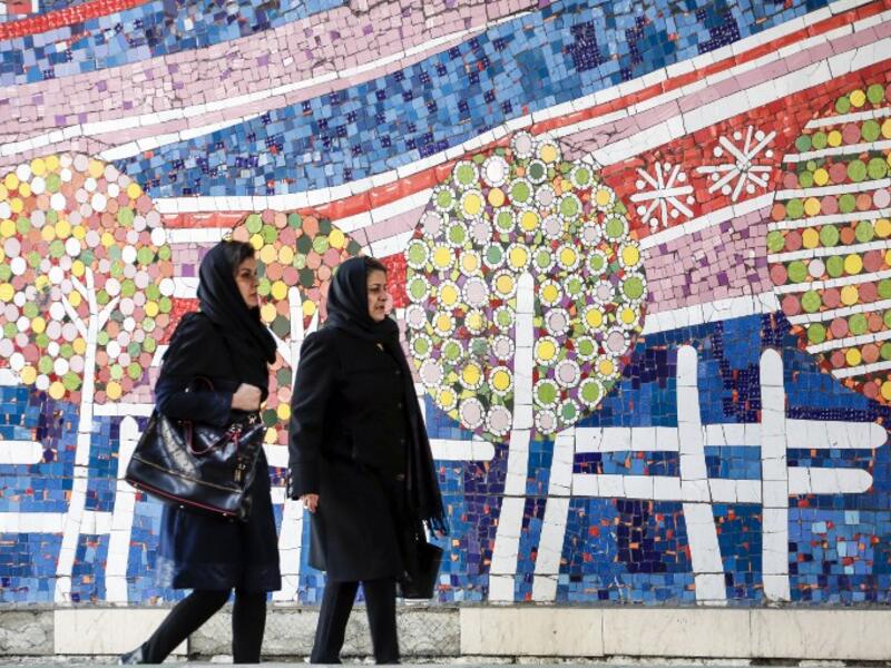 To women walks along a street past a mosaic mural on the first anniversary of the nuclear agreement in Tehran (Twitter)