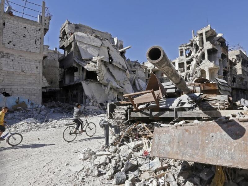 Boys ride their bicycle past a destroyed tank and buildings in the Palestinian camp of Yarmuk southern Damascus on November 1, 2018. 
LOUAI BESHARA / AFP