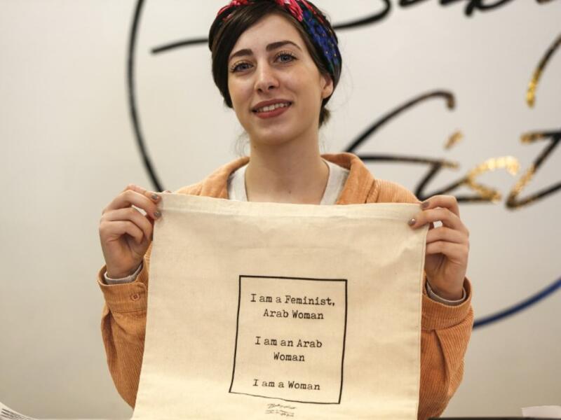 Amira Khader, Palestinian creative director of the feminist fashion label "BabyFist", poses with one of her canvas bags in her shop in Ramallah in the occupied West Bank 
ABBAS MOMANI / AFP