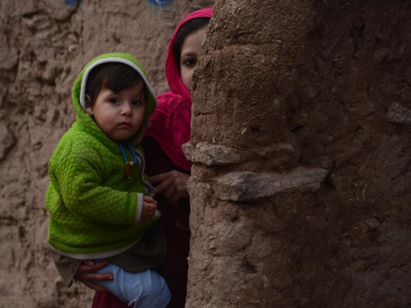 In this photograph taken on January 23, 2017, an Afghan girl holds her brother as she walks through a refugee camp in Herat. (AFP/Aref Karimi)