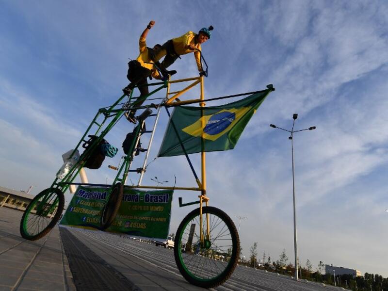 Brazilian football fans Elias de Souza and his son Elias de Souza junior perform acrobatics as they ride their homemade 3 metre-high tandem bicycle near Rostov Arena in Rostov-on-Don on June 16, 2018, on the eve of the match between Brazil and Switzerland during the Russia 2018 FIFA World Cup football tournament. 
JOE KLAMAR / AFP