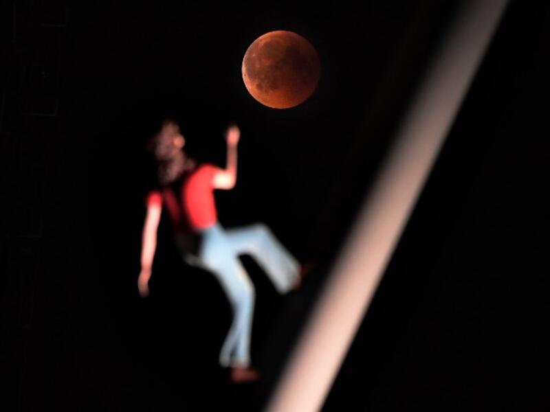 A "blood moon" eclipse is pictured with a sculpture by the American artist Jonathan Borofsky "Woman walking to the sky" on July 27, 2018 in Strasbourg, eastern France. (AFP/FREDERICK FLORIN)
