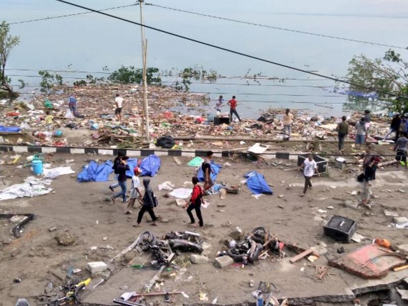People walk past dead bodies (blue cover) a day after an earthquake and a tsunami hit Palu, on Sulawesi island on September 29, 2018. (OLA GONDRONK / AFP)
