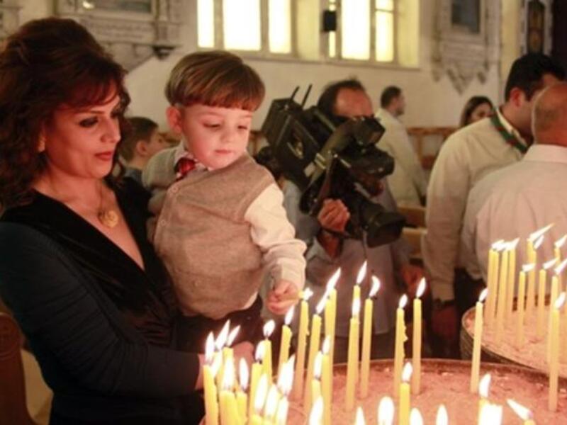 Syria's subdued celebrations in climate of unrest and fear still manage some cheering: A Christian Syrian woman holds her son as he lights a candle in Damascus while a cheering crowd waves palm leaves.