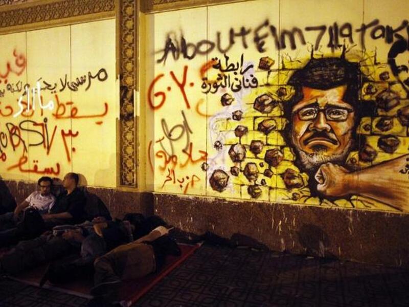 Egyptian opposition demonstrators calling for the ouster of President Mohamed Morsi sleep next to a wall covered in anti-Morsi graffiti (Mahmud Khaled / AFP)