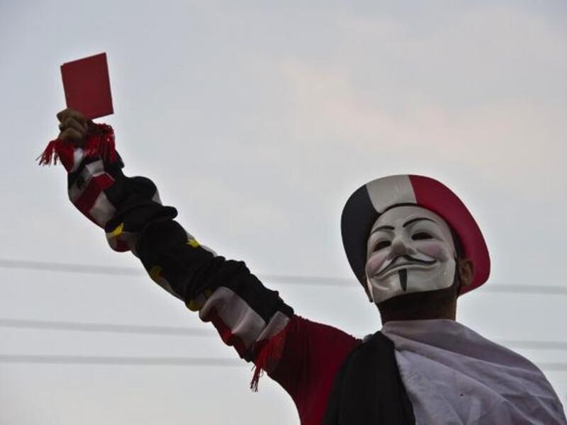 A protestor wearing a Guy Fawkes mask holds up a red card as thousands of Egyptian demonstrators gather outside the presidential palace in Cairo (Khaled Desouki / AFP)