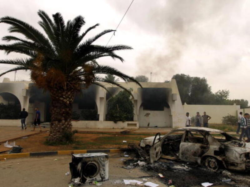 Libyan men stand outside a building used by Ansar al-Sharia militia after it was torched by residents on November 25, 2013 in Benghazi. [Abdullah Doma/AFP]