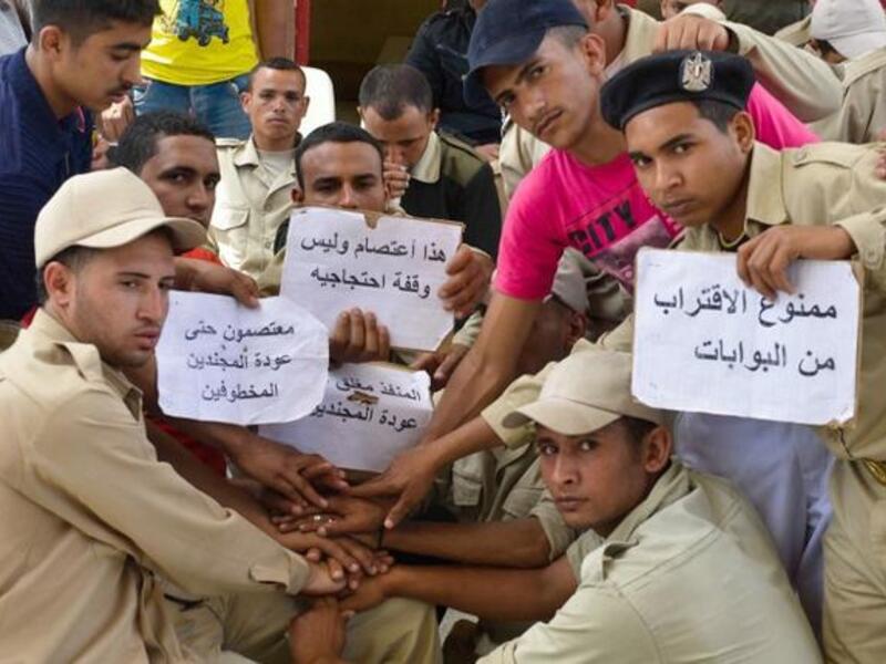 Egyptian police hold signs denoting that the gates are closed and demanding the return of their colleagues, as they gather at the Egyptian crossing point into the Gaza Strip (Mohamed el-Shahed/ AFP)