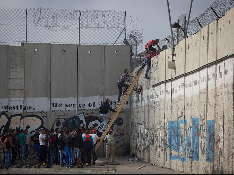 Palestinians climb over the barrier wall