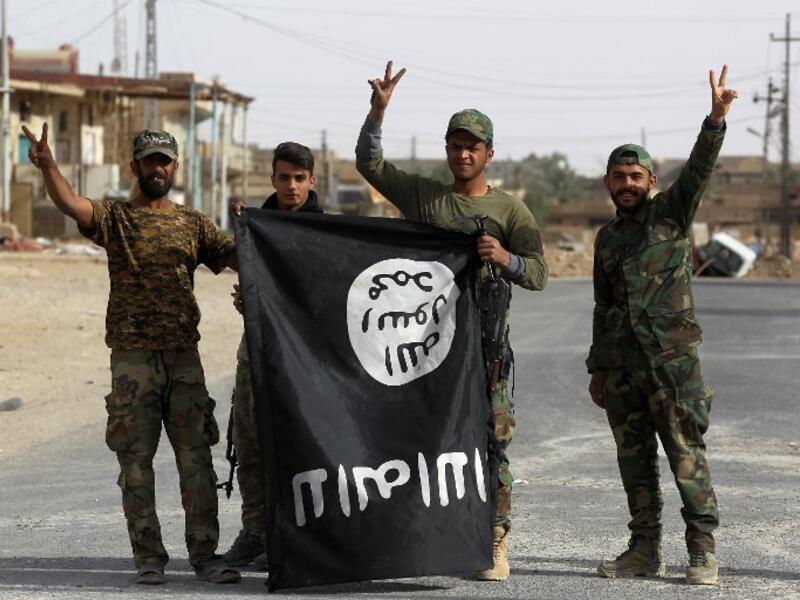 Iraqi members of the Hashed al-Shaabi (Popular Mobilisation Units) carry an upsidedown ISIS flag after victory in the city of al-Qaim (Ahmad Al-Rubaye/AFP)