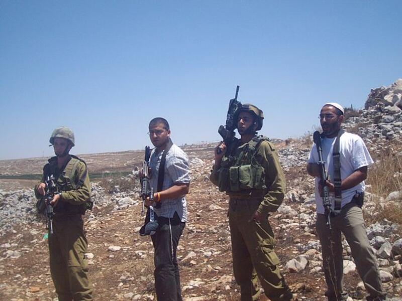 Armed Israeli settlers stand beside IDF soldiers in 2009 (Wikimedia Commons)