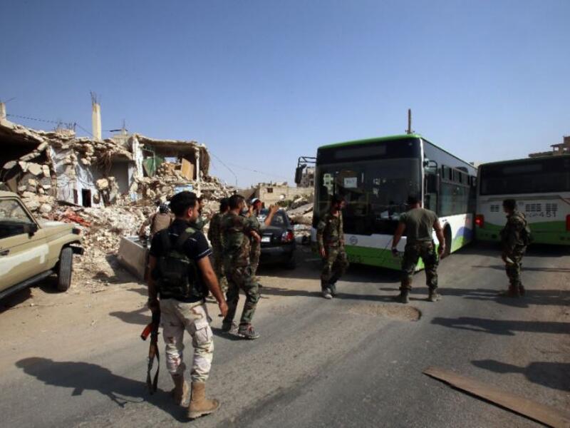 Syrian troops stand guard as a bus carrying people drives by, as part of an evacuation from the town of Daraya outside the capital Damascus on August 26, 2016 (AFP/Youssef Karwashan)
