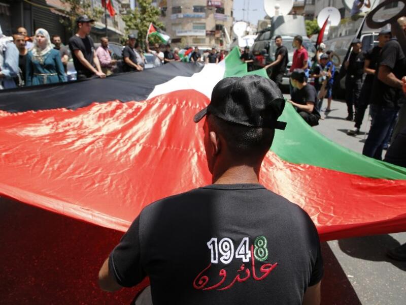 Palestinian protesters hold a large national flag as they take part in a protest marking the 69th anniversary of Nakba, near the West Bank city of Ramallah on May 15, 2017. (AFP/Abbas Momani)