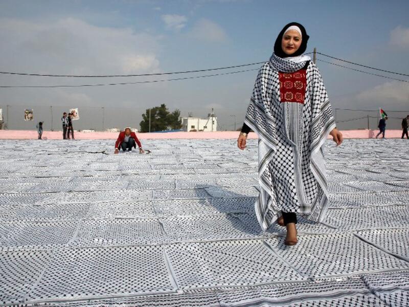 Palestinian Southern Education Direction's member Safa'a Amro (R) prepares a one thousand four hundred Meter square Keffiyeh. (HAZEM BADER / AFP)
