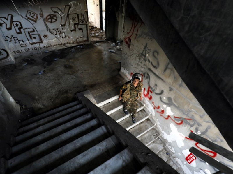A female fighter from the Kurdish People's Protection Units (YPG) descends stairs in an abandoned building in Raqa's eastern al-Sanaa neighbourhood, on the edge of the old city, on August 13, 2017 / AFP