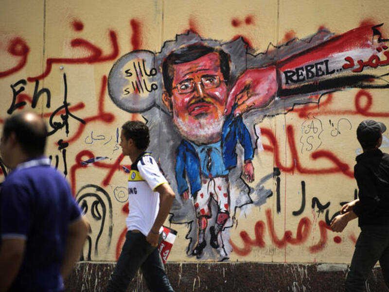 Egyptian protesters walk past graffiti against President Mohamed Morsi on the wall of the presidential palace in Cairo on July 1, 2013. (Source: AFP/GIANLUIGI GUERCIA)