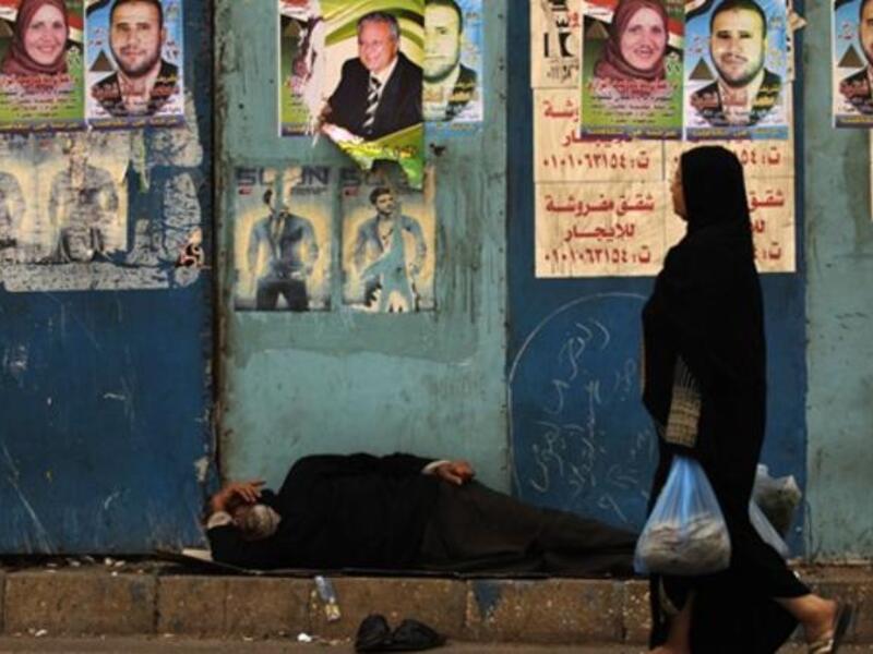An Egyptian woman walks past a man sleeping next to a wall decorated with election campaign posters next to a polling station in Cairo, as the nation of some 41 million eligible voters goes to the polls.