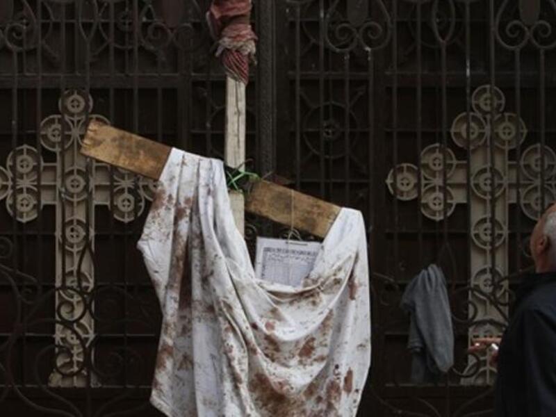 An Egyptian man stands next to a blood-stained peace of cloth hung outside the Al-Qiddisine church in the Mediterranean port city of Alexandria.