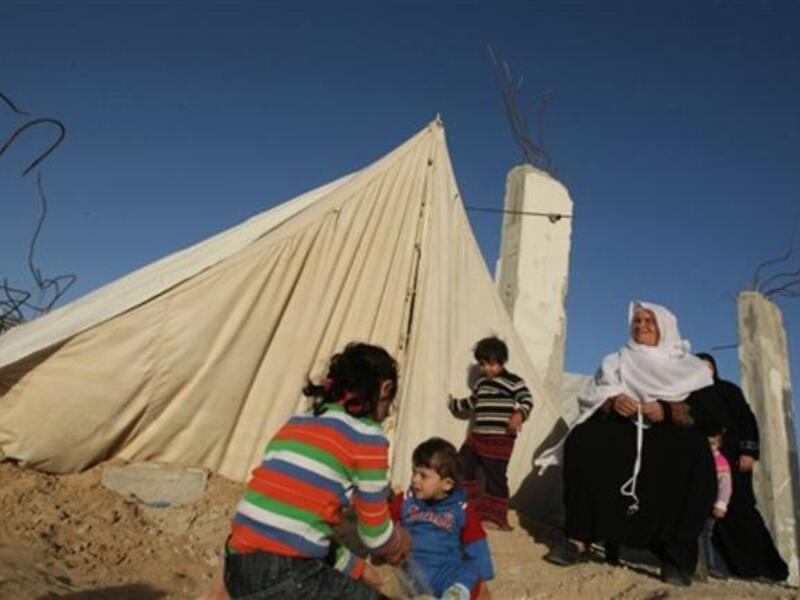 Members of a displaced Palestinian family sit outside their tent.
