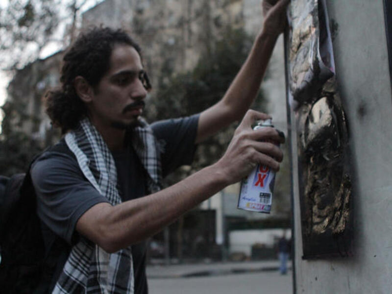 An Egyptian man spraying a graffiti paint on the the wall.