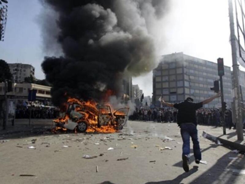 Supporters of the Future Movement gather as they watch the torched vehicle belonging to the Arabic language al-Jazeera satellite television station.