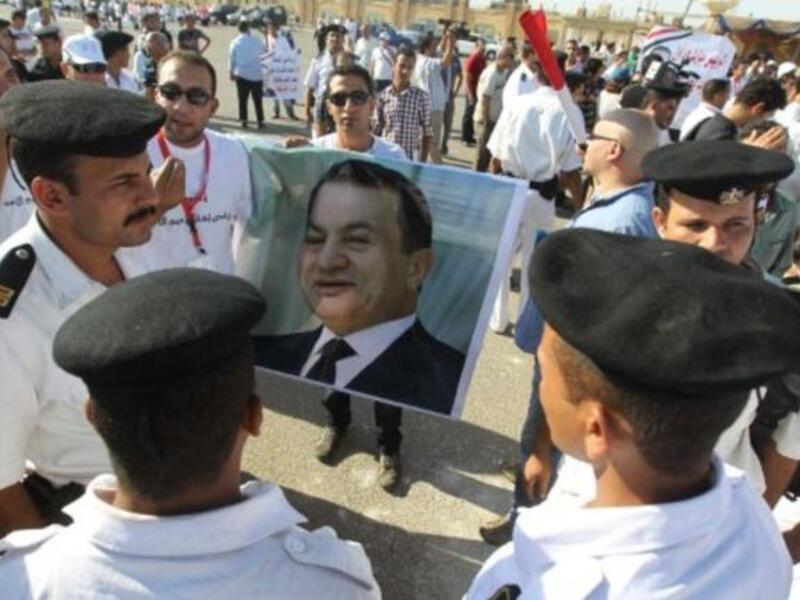 Egyptian supporters of former president Hosni Mubarak hold up his poster as they stand in front of the police on the opening day of his trial.