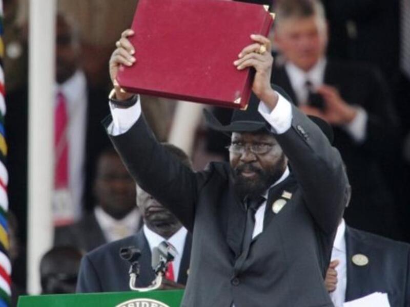 The President of Southern Sudan Salva Kiir waves the newly signed constitution of his country for the crowd to see.