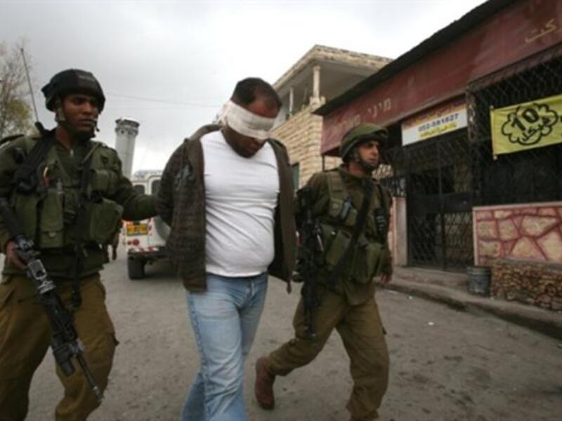 Israeli soldiers lead away a blind folded Palestinian man during a military operation at the entrance of the village of Beit Omar village in the Israeli occupied West Bank.