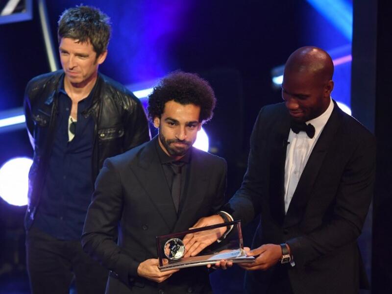 British singer-songwriter Noel Gallagher (L) and former Ivory Coast player Didier Drogba present Liverpool and Egypt forward Mohamed Salah (C) with the trophy for the FIFA Puskas Award for 2018, the best goal scored between July 2017 and July 2018 during The Best FIFA Football Awards ceremony, on September 24, 2018 in London. Ben STANSALL / AFP