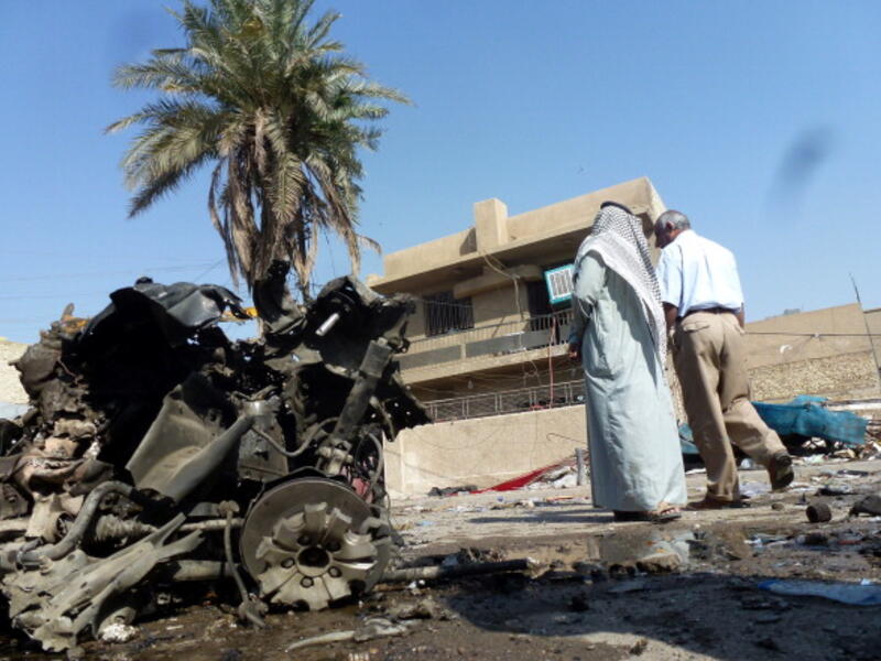Iraqis look at the remains of a vehicle following an explosion on October 27, 2013, in the the Mashtal district of the capital Baghdad. [SABAH ARAR/AFP/Getty Images]