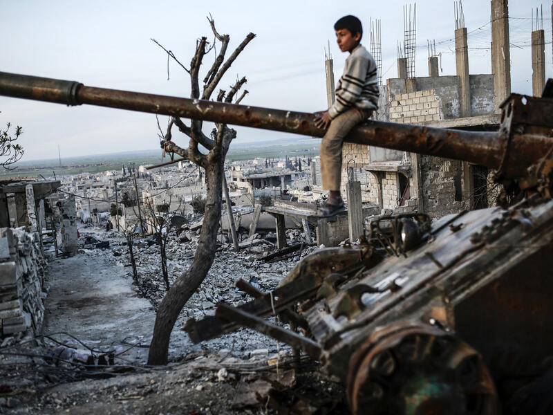 A boy sits on top of a destroyed tank in Syria, AFP/File