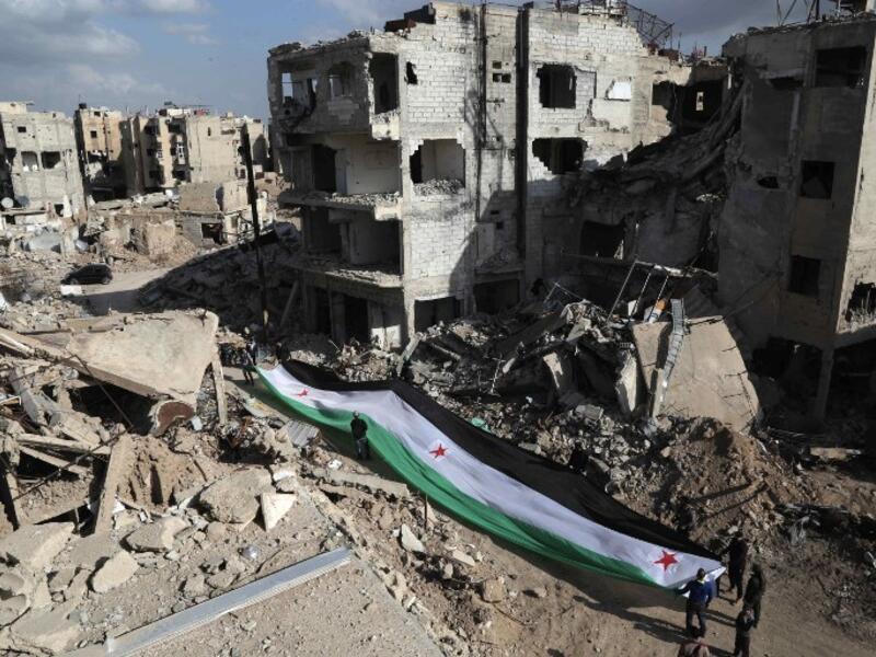 Residents and activists hold a giant a pre-Baath Syrian flag, now used by the Syrian opposition, during an anti-regime protest in the suburbs of Damascus. (AFP/Amer Almohibany)
