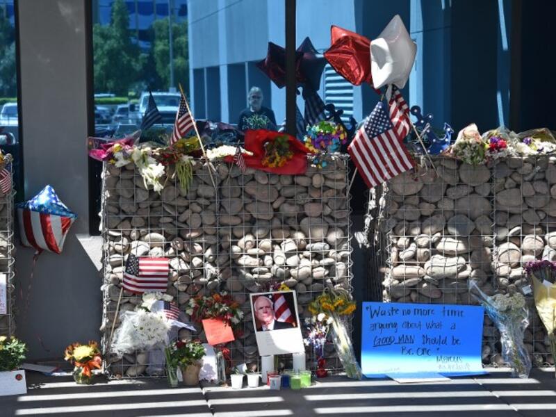 A passerby is reflected in glass as he collects himself before a makeshift memorial to Senator John McCain outside McCain's office in Phoenix, Arizona, August 27, 2018. McCain, a two-time US presidential candidate and war hero, passed away August 25 at the age of 81.  (Robyn Beck / AFP)