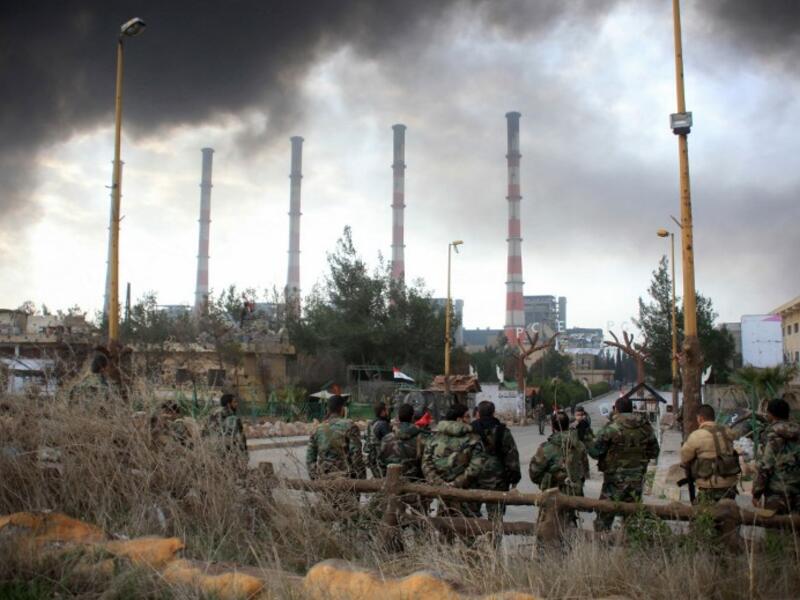 Syrian government forces watch smoke billowing from Aleppo's thermal power plant after taking control of the area on the eastern outskirts of the city from Daesh on February 21, 2016. 