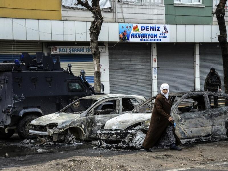 People walk past destroyed vehicles as they leave their houses during clashes in central Diyarbakir on March 15, 2016. (AFP/Ilyas Akengin)