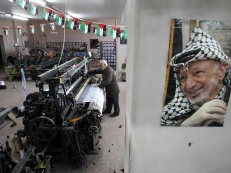 A poster of iconic keffiyeh-wearer Yasser Arafat overlooks as textile machines weave the scarves - symbols of Palestinian pride - at Hebron's Herbawi Textile Factory.  (AFP/Hazem Bader)