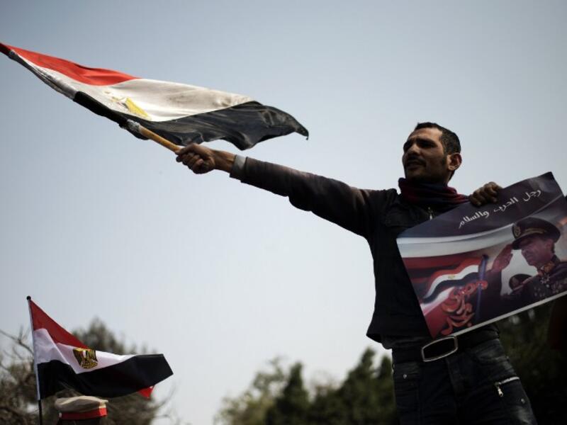 An Egyptian protestor waves his national flag while holding a poster of slain former Egyptian president Anwar Sadat with a slogan reading in Arabic "Man of war and peace" during a demonstration in support of the Egyptian army and against the Muslim Brotherhood. (AFP PHOTO/GIANLUIGI GUERCIA)