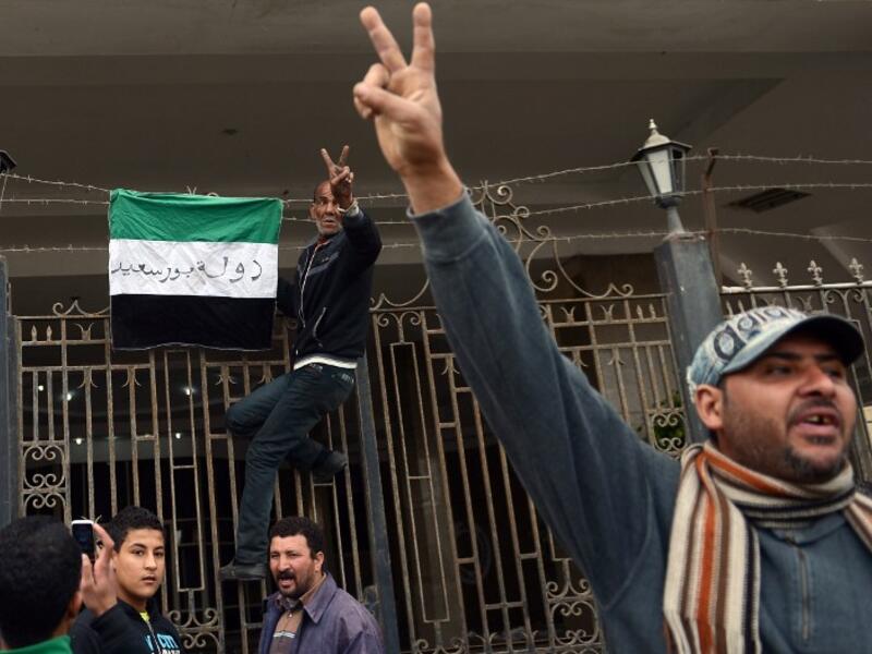 An Egyptian protestor flashes the sign for victory as he puts a flag with writing on it reading in Arabic: "state of Port Said" on the gate of the security headquarters, following the withdrawal of police forces from the main office. (AFP PHOTO / KHALED DESOUKI)