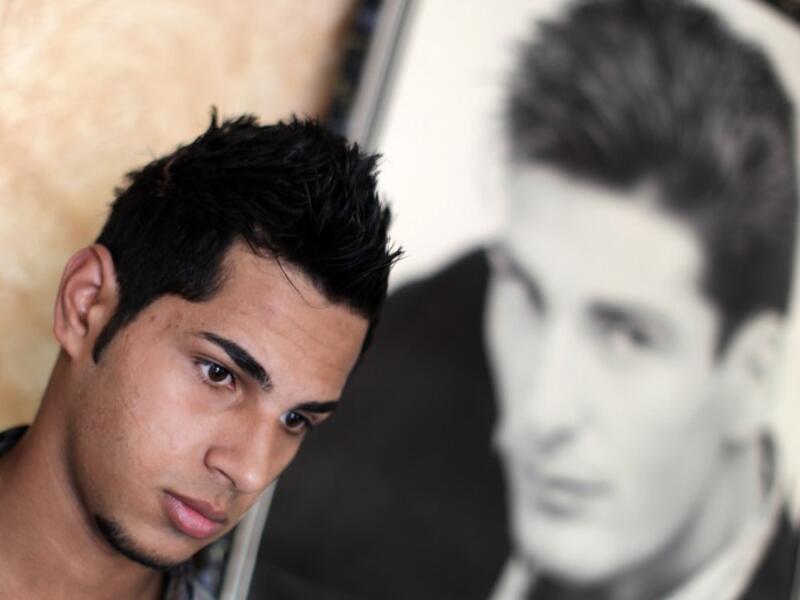 A Palestinian youth poses for a picture next to a poster after getting a stylish haircut at barber's shop in Gaza City. (AFP PHOTO/MAHMUD HAMS)