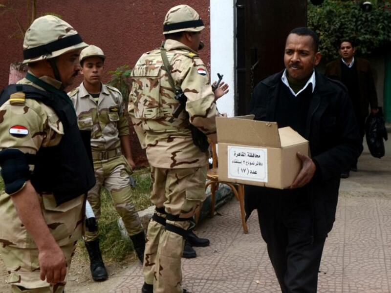 A man carries a box full of voting ballots near Egyptian soldiers standing guard outside a school that will be used as a polling station on January 13, 2014 in Cairo. [AFP]