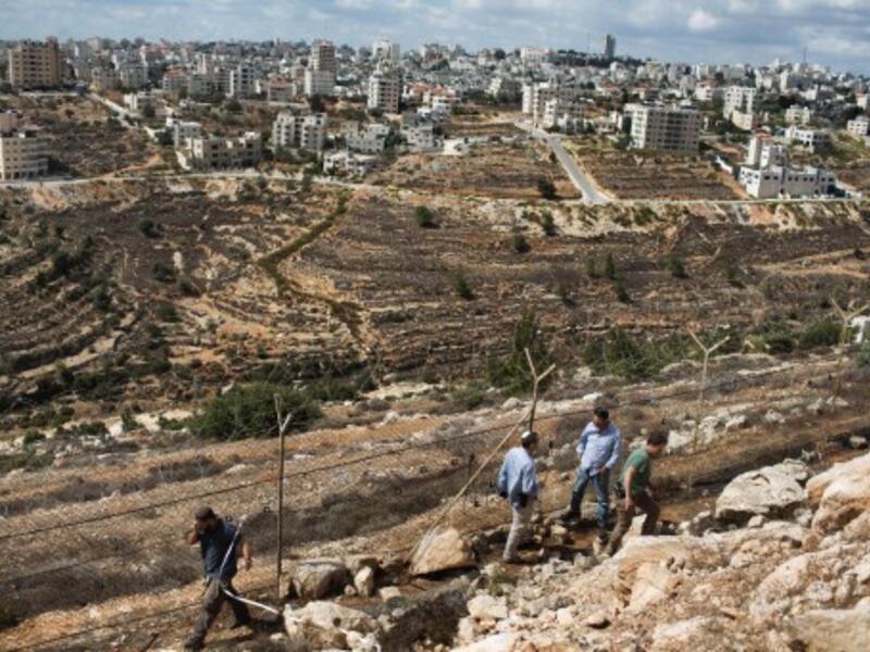 Armed Israeli settlers walk next to the fence between the Jewish settlement of Psagot and the Palestinian town of Al-Bireh (Back) on October 6, 2013 (AFP)