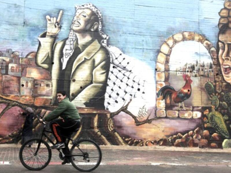A Palestinian boy cycles past a mural painted by university students depicting the late Palestinian leader Yasser Arafat in the West Bank city of Nablus on November 9, 2013. (AFP)