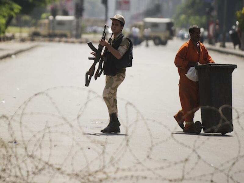 An Egyptian army soldier holds his rifle as he walks by a street cleaner behind a barbed wire checkpoint on a street in Cairo on August 23, 2013. (AFP)