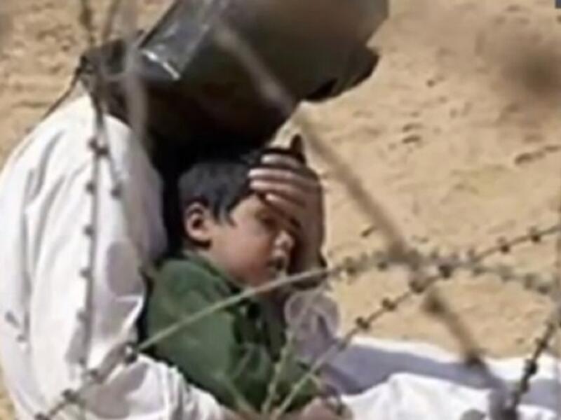  صورة المسجون العراقي الذي حاول حماية طفلة 4 سنوات من حرارة الشمس الحارقة بعدما فك سجانوه قيوده، ولكنهم منعوه من رؤية طفله ووضعوا على رأسه الغطاء .