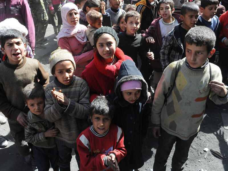 Palestinian children stand during a relief operation in Syria's besieged Yarmouk refugee camp, February 24, 2014. (AFP/SANA)