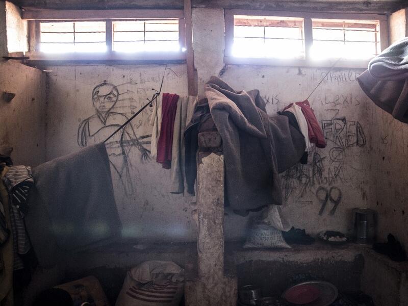 This picture shows blankets and clothes of South Sudanese refugees hanging in front of a wall filled with drawings and writings depicting scenes from home in a refugee transition camp for refugees who have just arrived in Aru. JOHN WESSELS / AFP