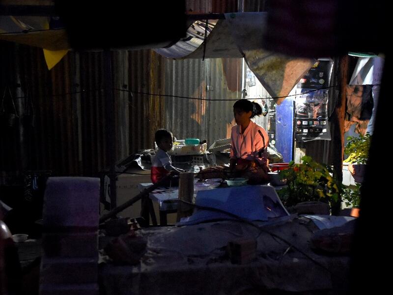 This picture  shows a woman and her child preparing dinner next to graves outside their home in Phnom Penh.  TANG CHHIN Sothy / AFP
